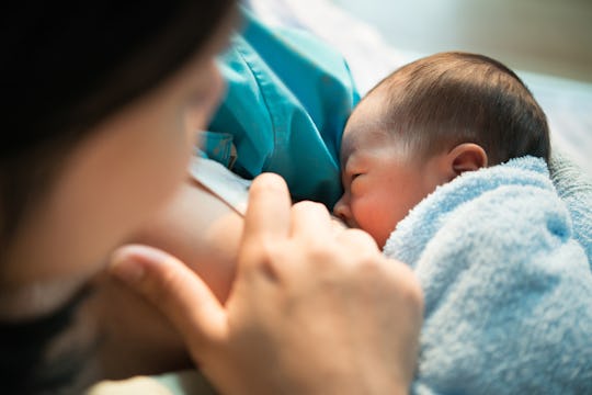 close-up of mom breastfeeding newborn with blue blanket, in an article answering the question, is it...