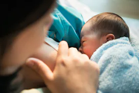 close-up of mom breastfeeding newborn with blue blanket, in an article answering the question, is it...