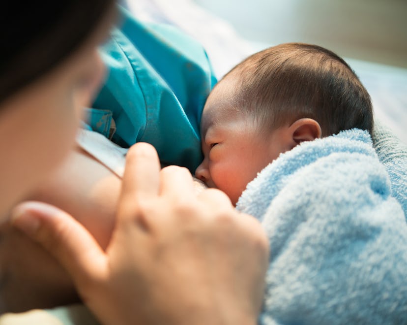 close-up of mom breastfeeding newborn with blue blanket, in an article answering the question, is it...