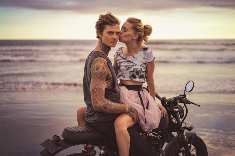 girlfriend kissing boyfriend on motorcycle on ocean beach during beautiful sunrise