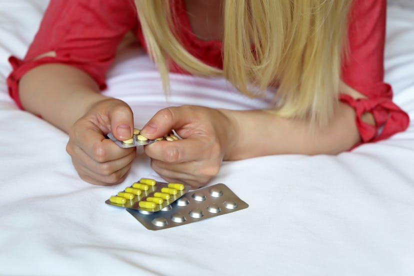 Woman with pills, female hands on the bed with a blister pack of tablets. Blonde girl taking medicat...