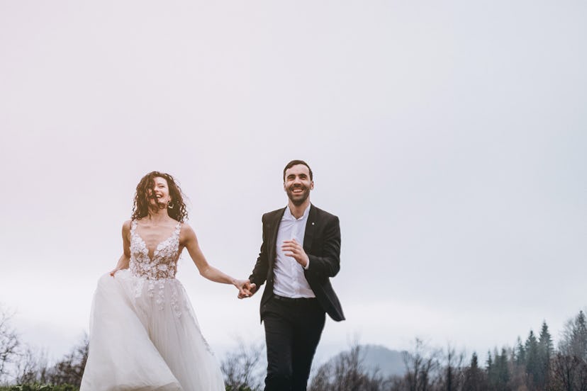 a man and a woman who run by holding hands against a white skies background. Happy and lovely couple...