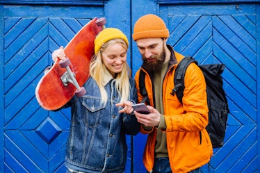 Happy american hipster friends longboarders showing something in smartphone on blue wooden backgroun...