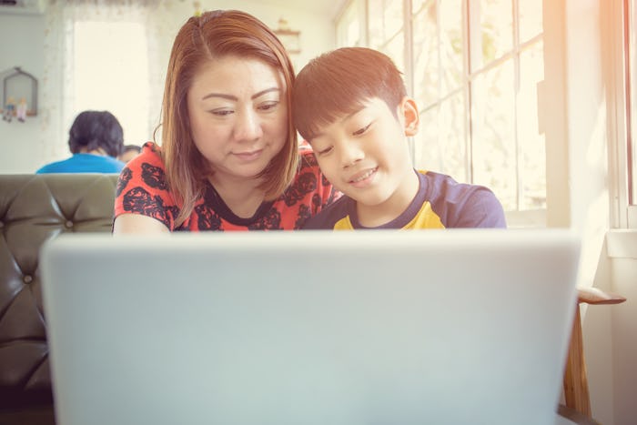 Happy Asian Mother And Son Sitting At Desk Using Laptop At Home 