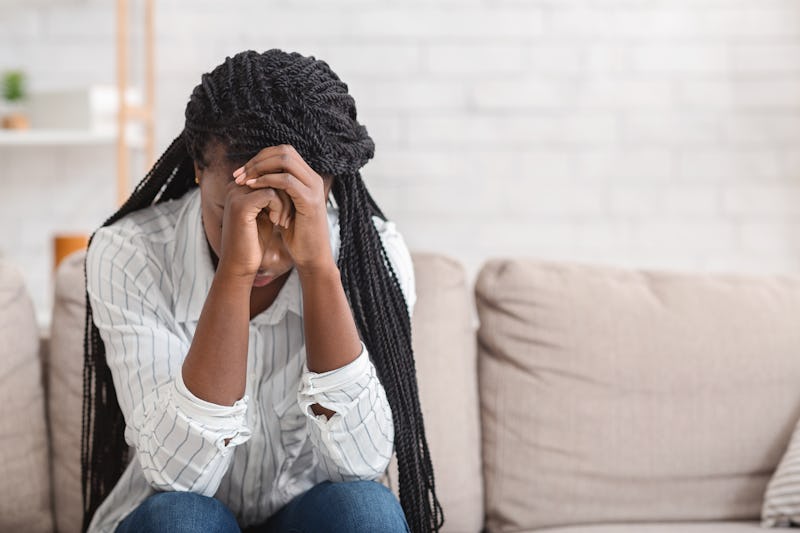 Despair. Upset black woman sitting alone at home, touching her head in despair, selective focus