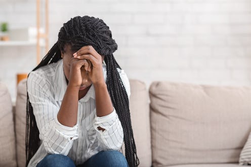 Despair. Upset black woman sitting alone at home, touching her head in despair, selective focus