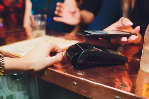 Mid-section of woman paying bill through smartphone using NFC technology in cafe.