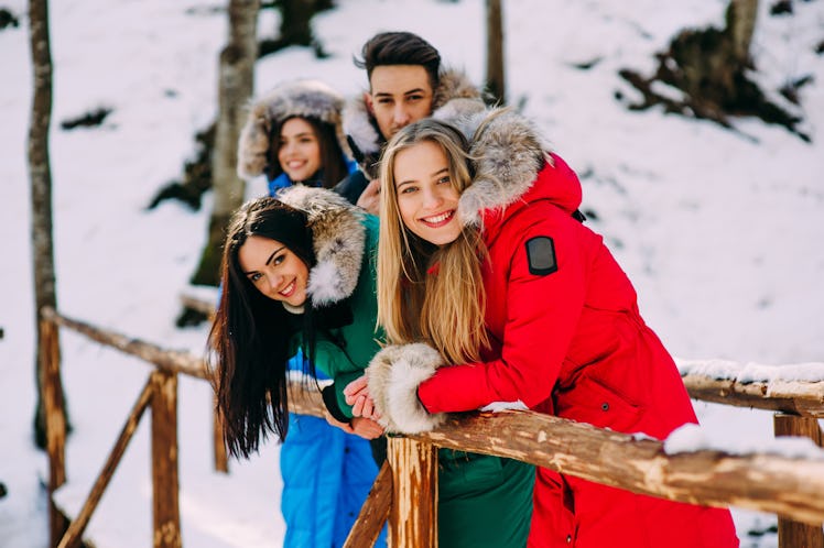 friends, three girls and one boy standing on a wooden bridge in the forest in winter