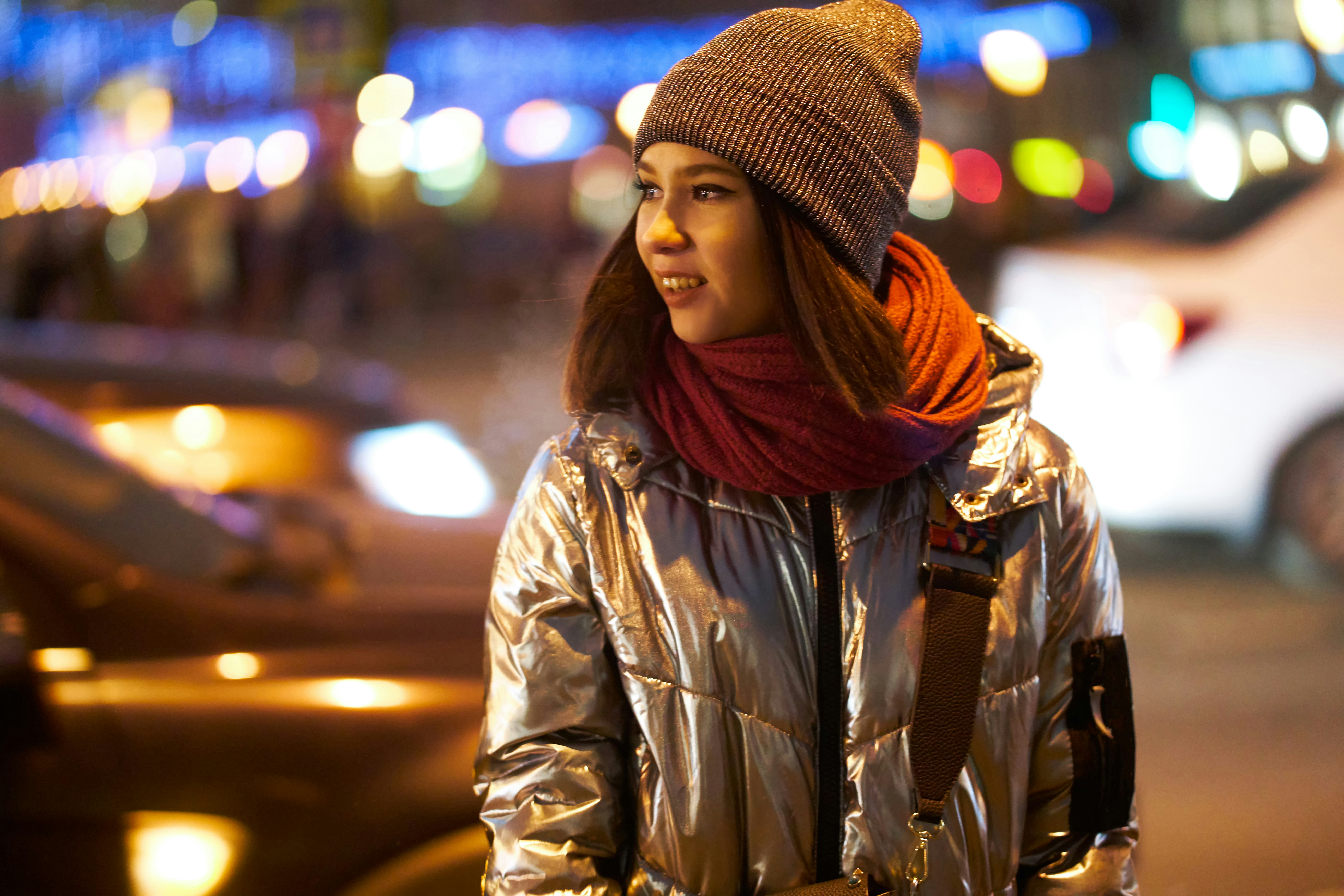 girl in a winter jacket a red scarf and hat. on the background of Christmas lights. bokeh Garlands. ...