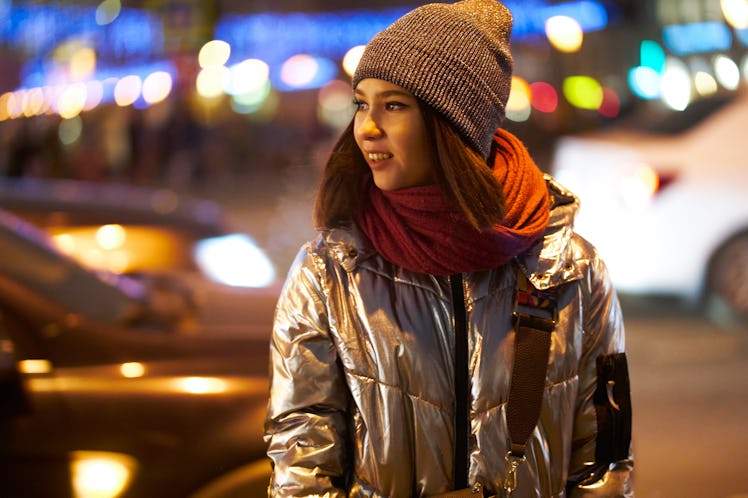 girl in a winter jacket a red scarf and hat. on the background of Christmas lights. bokeh Garlands. ...