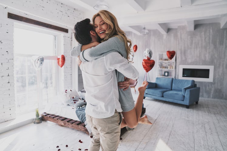 A couple hugs and laughs while celebrating a birthday in their bedroom that's filled with balloons a...