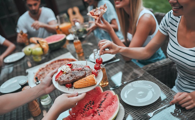 A group of friends sits and eats around a table during a birthday barbecue in the summer.