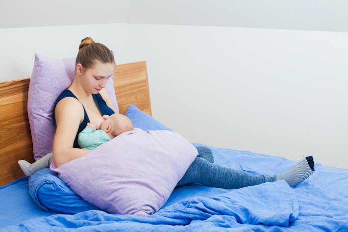 Mother feeding baby sitting on bed in the bedroom