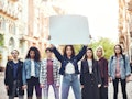 Girl power. Group of young women standing on the road during protest march. Young woman holding blan...