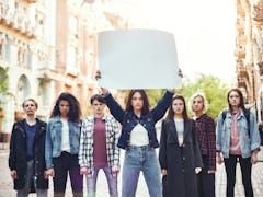 Girl power. Group of young women standing on the road during protest march. Young woman holding blan...