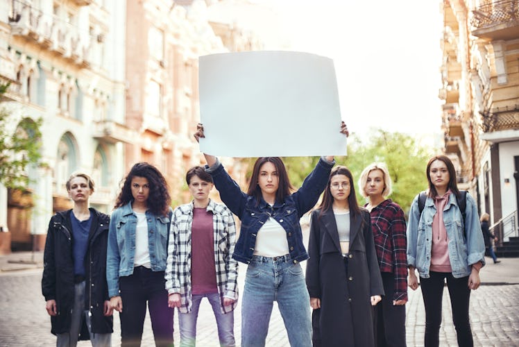 Girl power. Group of young women standing on the road during protest march. Young woman holding blan...
