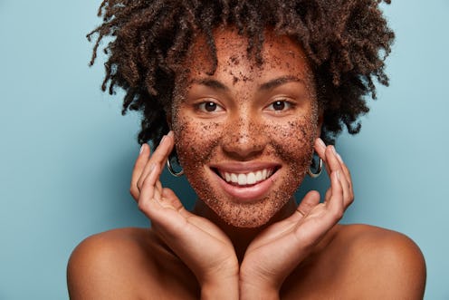 Photo of smiling black woman has cleansing mask or scrub on face, smiles broadly, enjoys beauty trea...