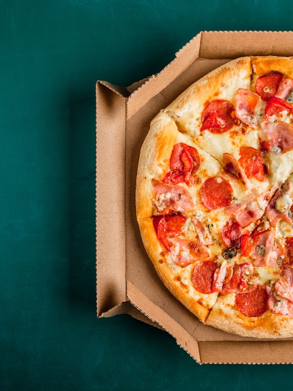 Pizza in a cardboard box on a green chalkboard background. Space for text. View from above. Pizza de...