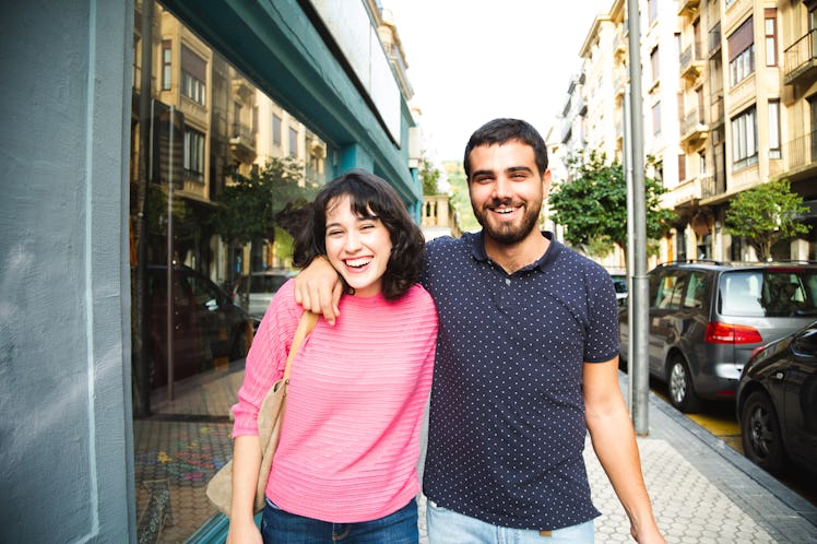 A happy couple walks down a city street on a sunny day and laughs.