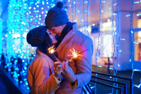 Christmas and New year fun concept. Couple in love burning sparklers by holiday illumination outdoor...