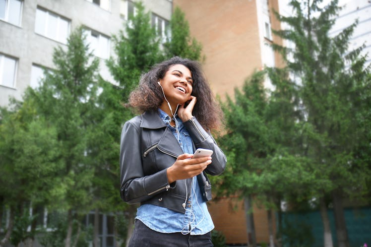 Beautiful young African-American woman listening to music outdoors