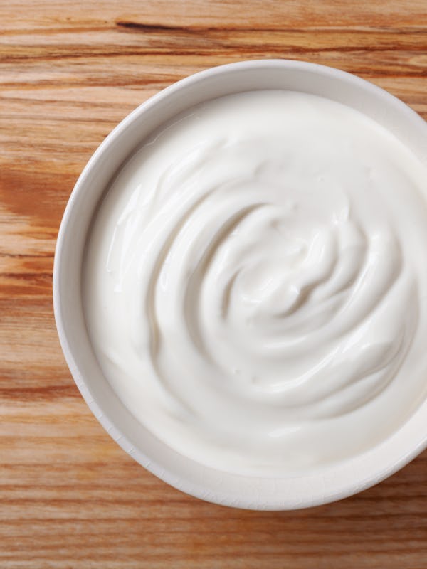 Greek yogurt in white bowl on wooden table top view.