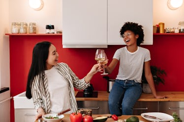 Funny friends laugh and clink glasses with champagne in kitchen