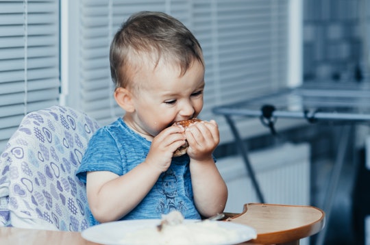 little boy eating chicken in high chair