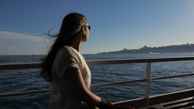 happy woman in sunglasses with waving hair travels by ship and enjoys magnificent seascape under sun...