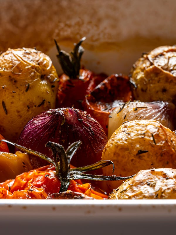 Roasted potatoes, vine ripe tomatoes and pearl onions in a ceramic roasting dish