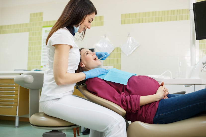 Pregnant woman laying on dental chair while dentist checking her teeth