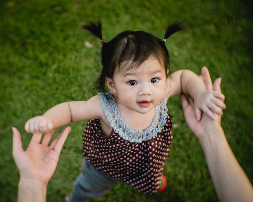 baby girl taking first steps holding mom's hands