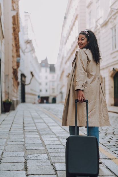 A happy woman rolls her suitcase down a city street in Europe while on vacation.