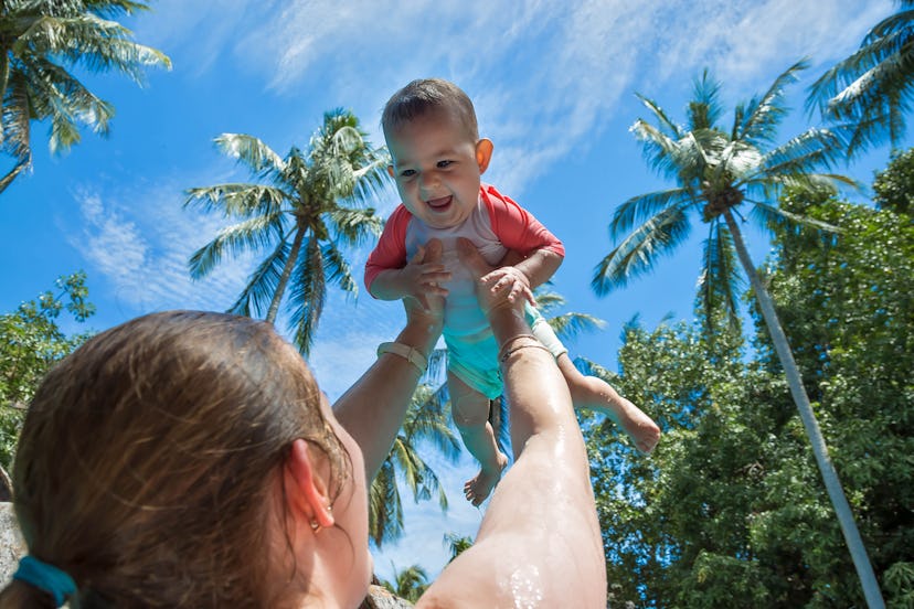 Mom raised baby high above the head in the pool. The little girl is very happy and screams for joy. ...