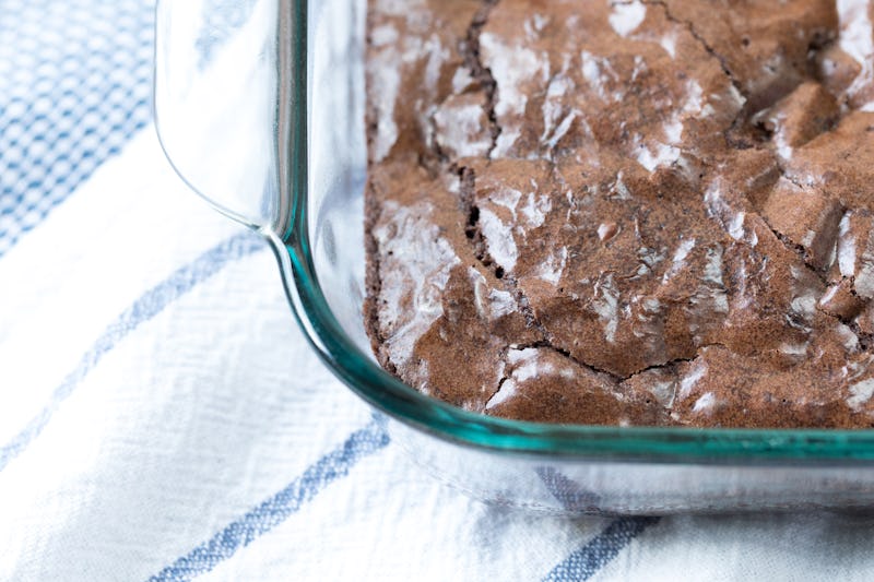 Overhead perspective on corner of cracked brown surface of freshly homemade baked chocolate chip chunk brownies in glass pan container on white and blue stripe linen table cloth in window light