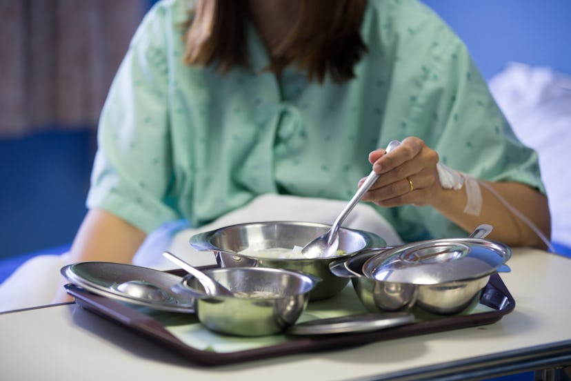 Patient woman is on drip receiving a saline solution with cooked rice and other food in stainless bo...