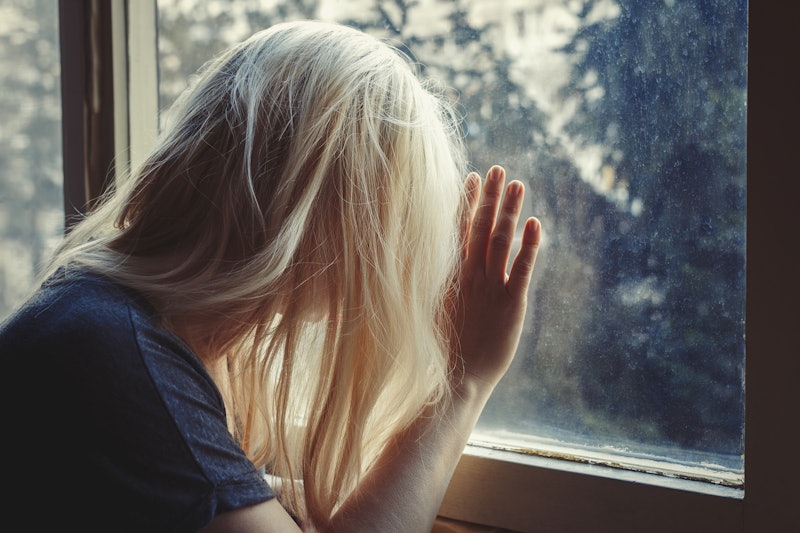 Blonde haired woman leaning against window, looking out, sad, depressed and lonely with unbrushed lo...
