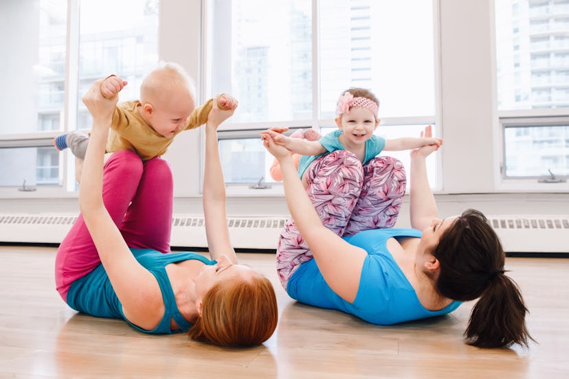 Group of two young women with children doing workout in gym class to loose baby weight. Child-friend...