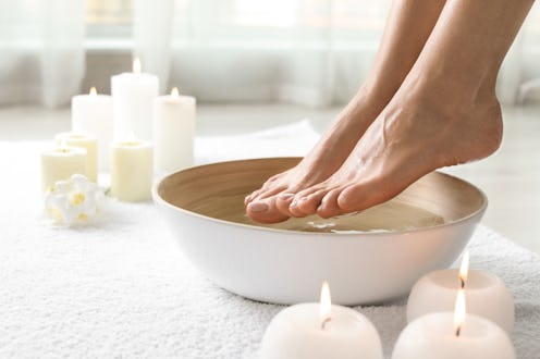 Woman soaking her feet in dish indoors, closeup with space for text. Spa treatment
