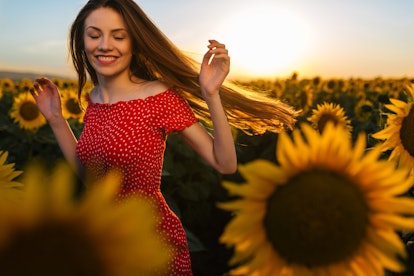 A woman spins around in a sunflower field with a red dress on. 