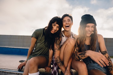 Shot of three smiling girls hanging out at skate park. Group of women friends sitting outdoors at sk...