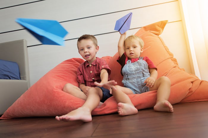 Two little boys playing with paper airplanes at home.