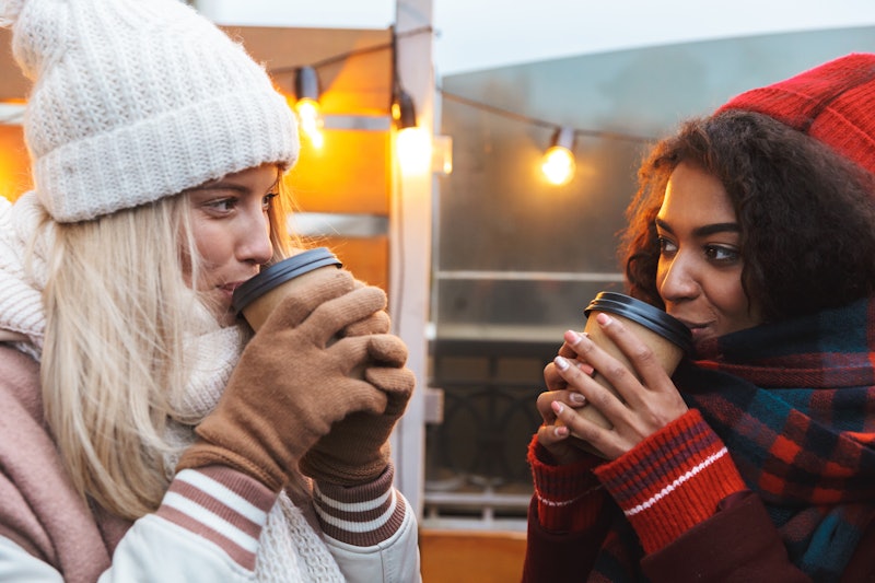Image of a happy young friends girls talking with each other drinking coffee outdoors winter concept...
