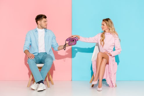 couple sitting on chairs and holding purple vintage telephone on pink and blue background