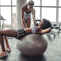 Trainer helping client workout on exercise ball at the gym. Wellness concept