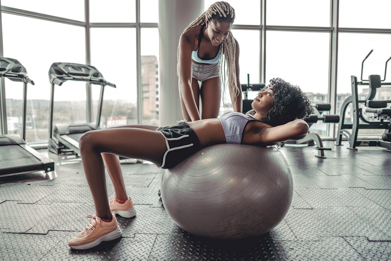 Trainer helping client workout on exercise ball at the gym. Wellness concept