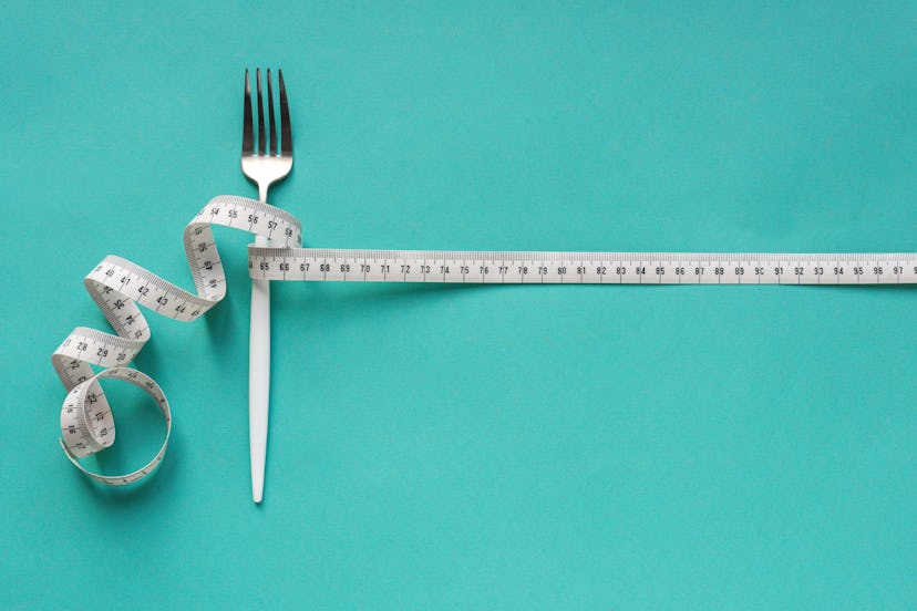 Fork and Measuring Tape on blue background, copy space. Diet, healthy lifestyle, weight loss concept...