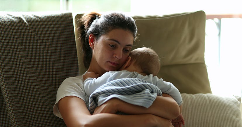 
Tired mother holding and caring for baby infant on couch. Exhausted mom falling asleep, candid and ...