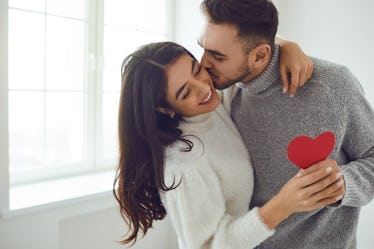 A guy kisses his girlfriend and gives her a red paper heart on Valentine's Day.