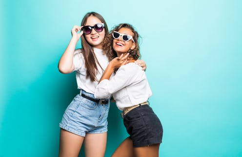 Friends forever. Two cute lovely girl friends in sunglasses posing with smile on blue background